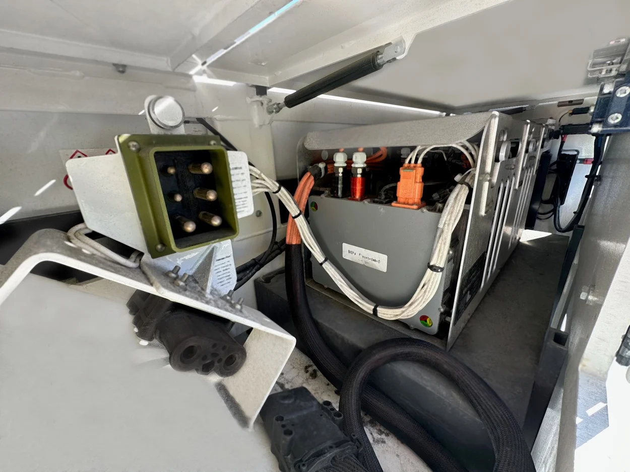 Open equipment compartment on an electric ground support unit showing an onboard charger, orange high-voltage connectors, and routed cabling.